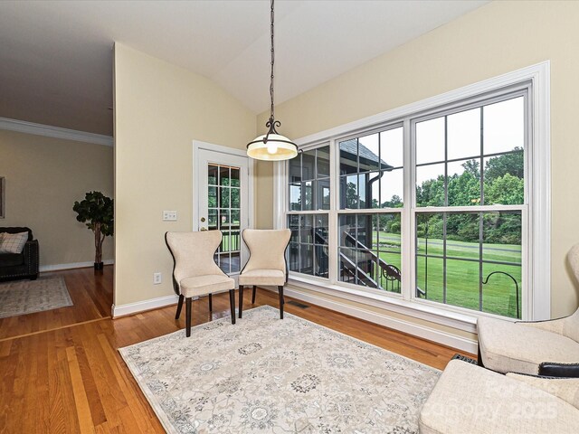 living area with wood finished floors, baseboards, lofted ceiling, and crown molding