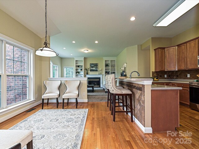 kitchen featuring open floor plan, stainless steel range with electric cooktop, a fireplace, wood finished floors, and hanging light fixtures