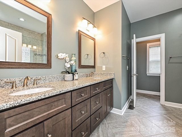 full bath featuring baseboards, tiled shower, and double vanity