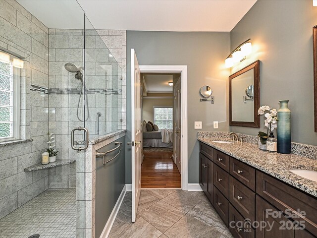 full bathroom with ensuite bath, a shower stall, double vanity, baseboards, and marble look tile flooring