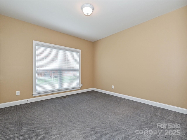 spare room featuring dark carpet and baseboards