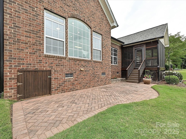 view of front facade with a sunroom, a patio, roof with shingles, brick siding, and a front lawn