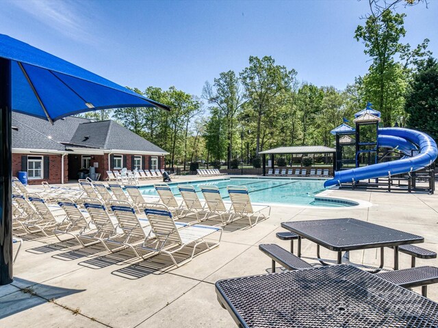 community pool featuring a water slide, a patio, fence, and view of wooded area