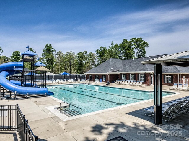 community pool featuring a water slide, fence, and a patio area
