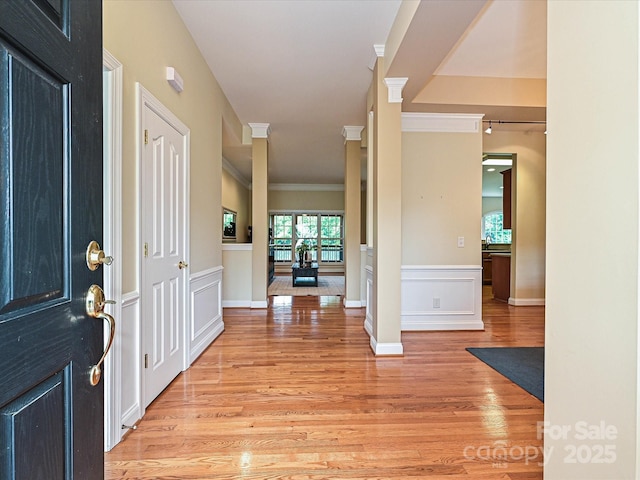 entrance foyer with crown molding, light wood-type flooring, ornate columns, and wainscoting