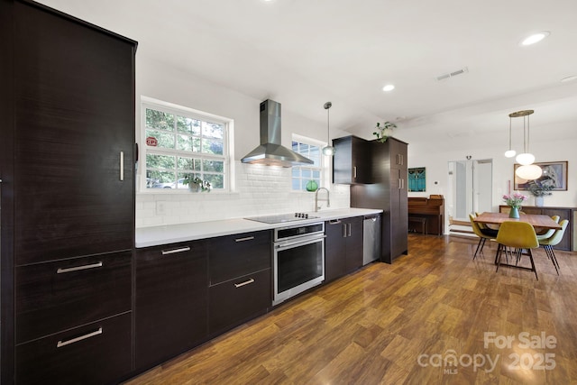 kitchen featuring visible vents, wall chimney range hood, light countertops, appliances with stainless steel finishes, and backsplash