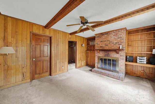 unfurnished living room with wood walls, carpet, a textured ceiling, beamed ceiling, and built in features