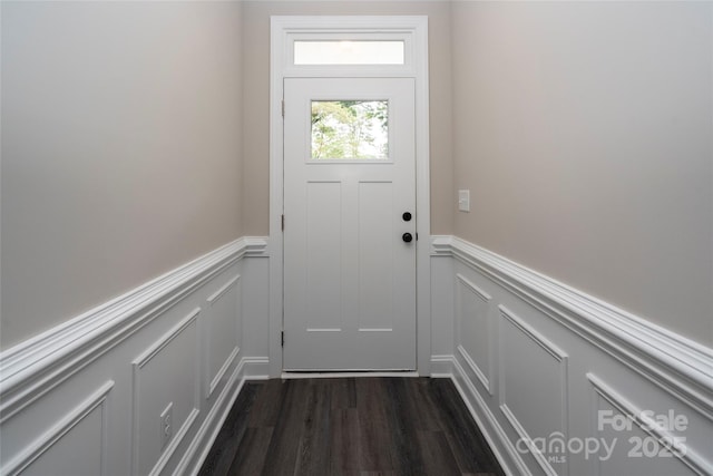 doorway to outside featuring dark wood finished floors, a wainscoted wall, and a decorative wall