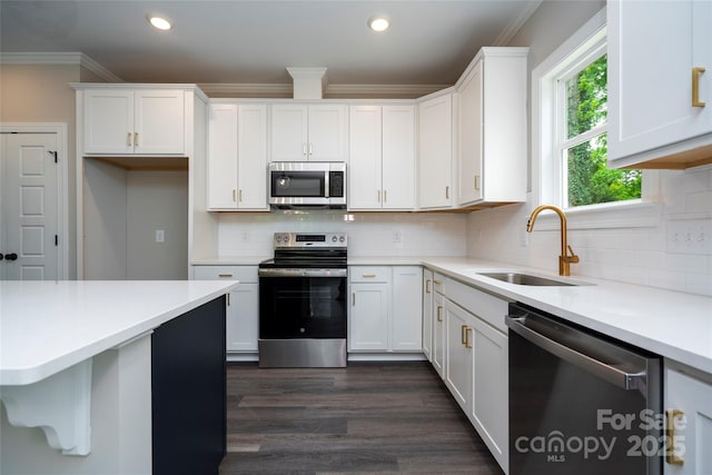 kitchen featuring stainless steel appliances, light countertops, white cabinets, a sink, and crown molding