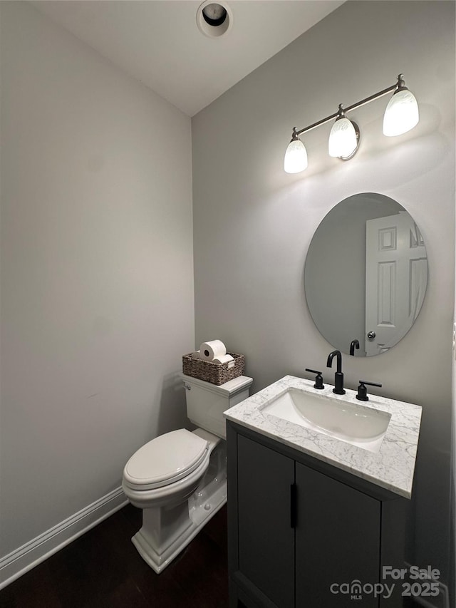 half bathroom with vanity, baseboards, and toilet
