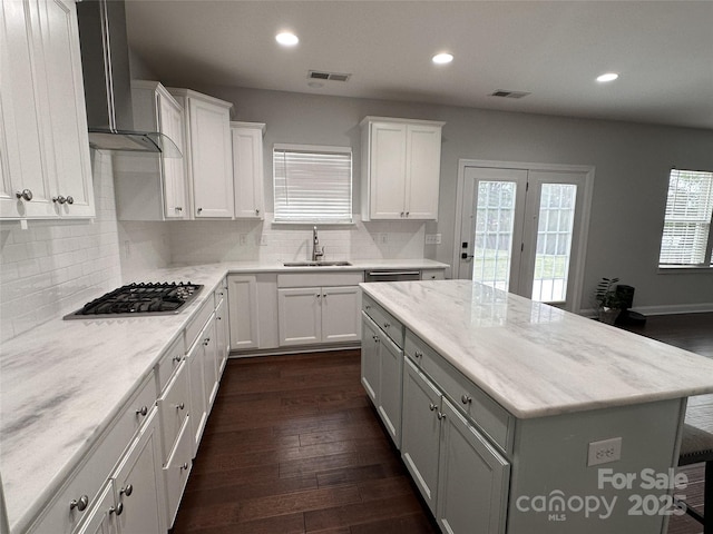 kitchen with a sink, stainless steel gas stovetop, wall chimney exhaust hood, and visible vents