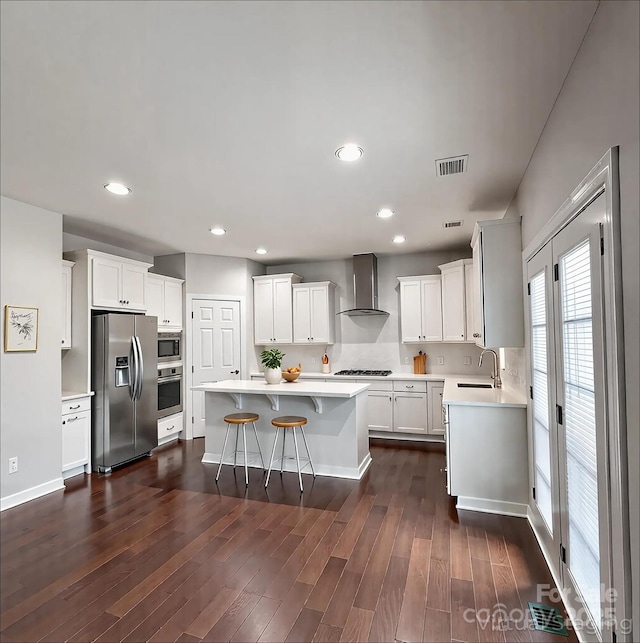 kitchen with wall chimney range hood, a kitchen island, visible vents, appliances with stainless steel finishes, and a sink