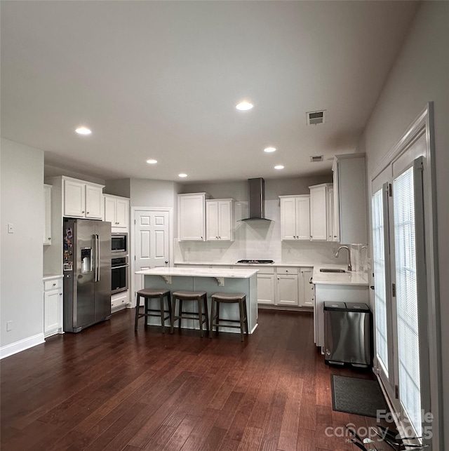 kitchen featuring dark wood-style flooring, visible vents, wall chimney exhaust hood, appliances with stainless steel finishes, and a sink