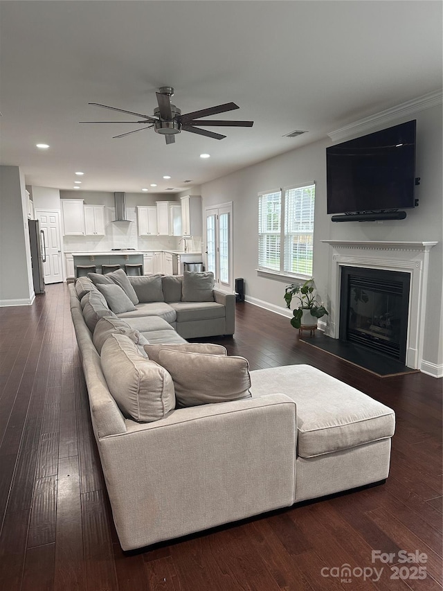 living area with a glass covered fireplace, baseboards, dark wood-style floors, visible vents, and ceiling fan