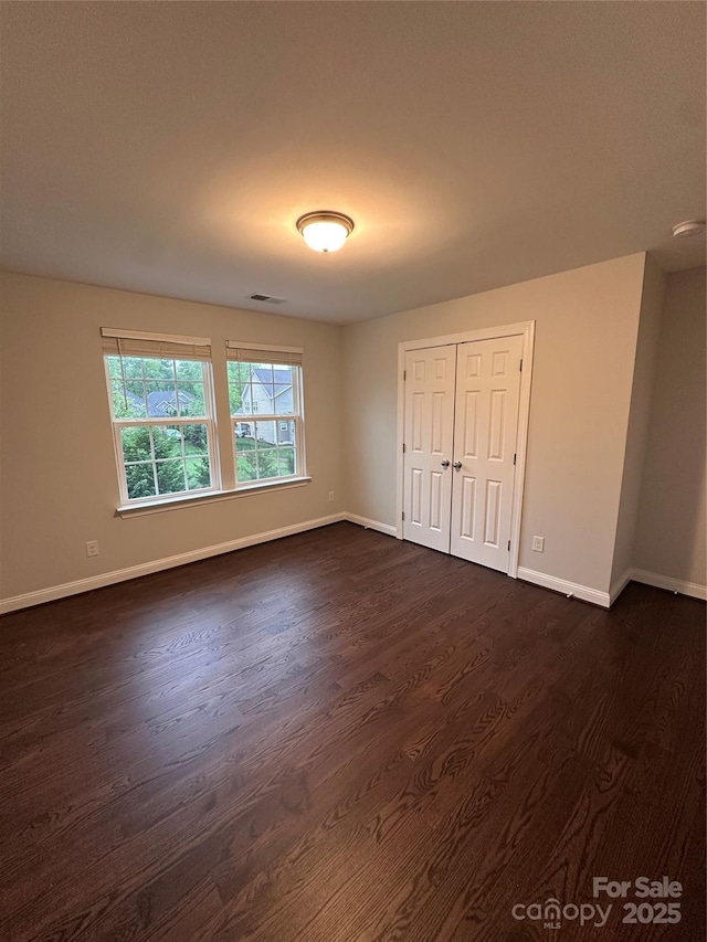 unfurnished bedroom with dark wood-type flooring, a closet, baseboards, and visible vents