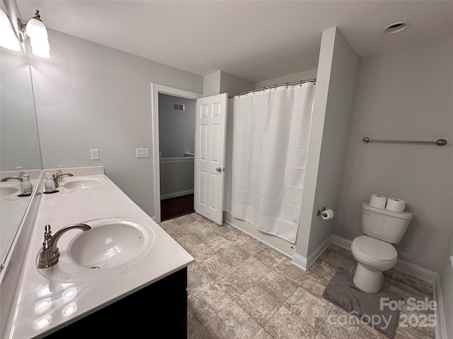 full bath featuring toilet, double vanity, a sink, and baseboards