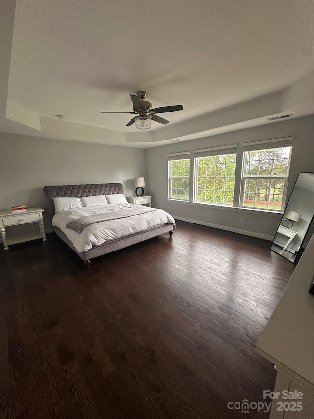 unfurnished bedroom featuring a tray ceiling, baseboards, visible vents, and dark wood finished floors