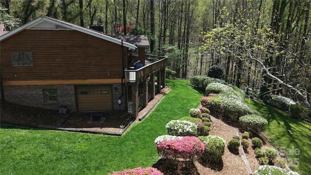 view of yard with an attached garage, a view of trees, and a deck