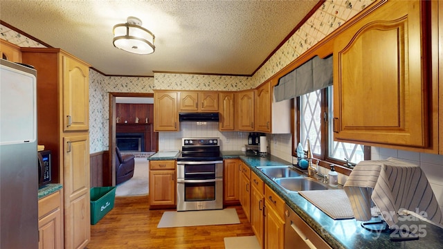 kitchen featuring wallpapered walls, ornamental molding, under cabinet range hood, stainless steel appliances, and a sink
