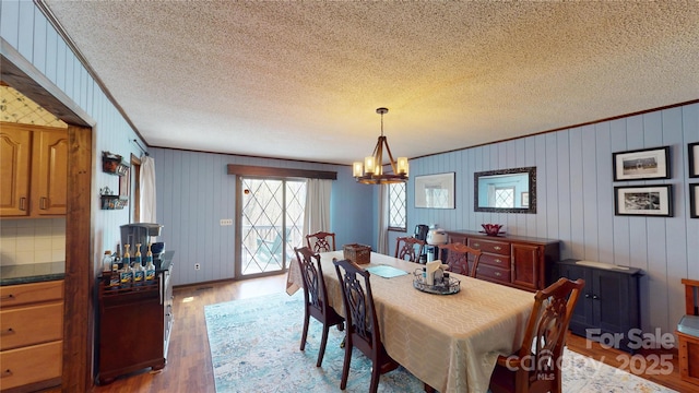 dining space with ornamental molding, an inviting chandelier, light wood-style floors, and a textured ceiling
