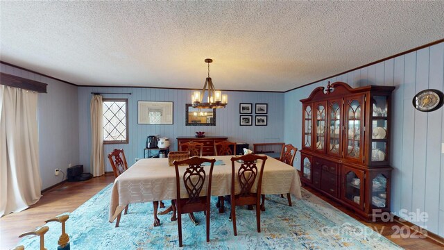dining space with light wood-style flooring, a textured ceiling, a notable chandelier, and ornamental molding