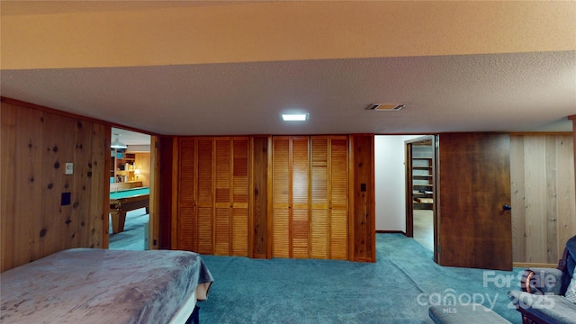 carpeted bedroom with a textured ceiling, wooden walls, billiards, and visible vents