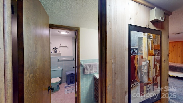 hallway with tile walls, a wainscoted wall, visible vents, and a textured ceiling