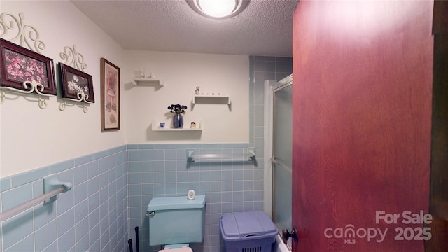 full bath featuring wainscoting, a textured ceiling, tile walls, and toilet