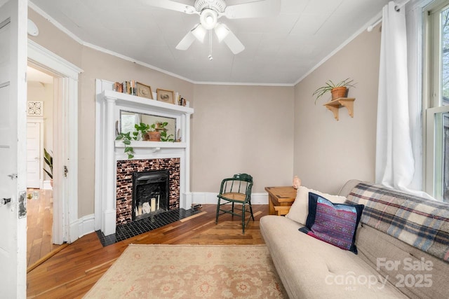 living area with crown molding, wood finished floors, a fireplace, and a ceiling fan