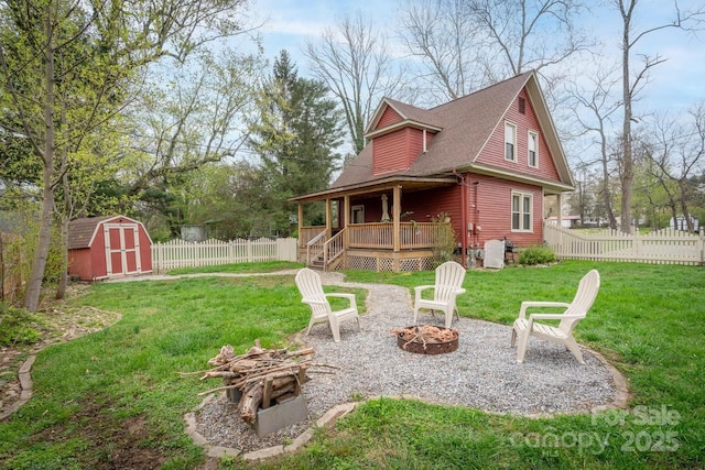 back of house with a deck, an outdoor fire pit, a lawn, an outdoor structure, and a storage unit
