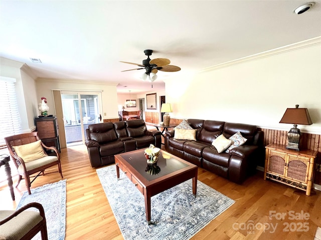 living room with a wealth of natural light, visible vents, ornamental molding, and a ceiling fan