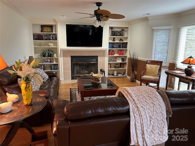 living room featuring a tile fireplace, a ceiling fan, visible vents, built in shelves, and wood finished floors