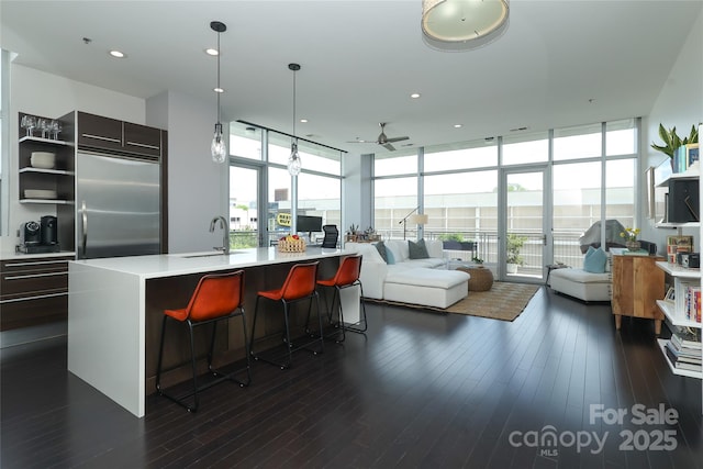 living area with a wealth of natural light, expansive windows, dark wood-style floors, and a ceiling fan
