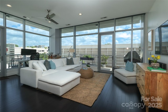living area featuring dark wood-type flooring, visible vents, a ceiling fan, and expansive windows