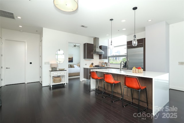 kitchen featuring light countertops, visible vents, wall chimney exhaust hood, appliances with stainless steel finishes, and a sink
