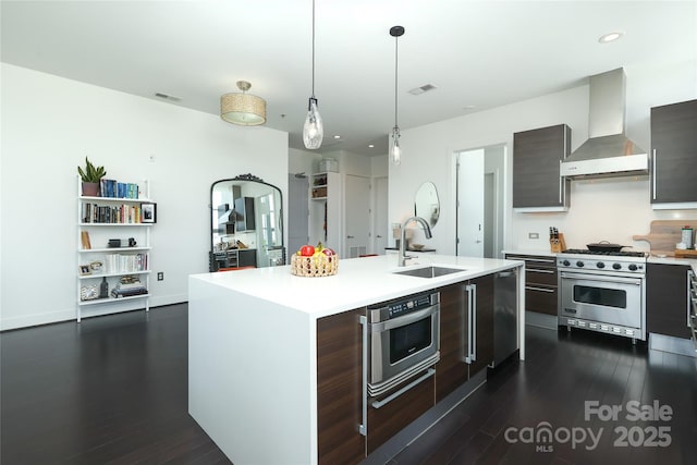 kitchen with stainless steel stove, light countertops, dark wood-type flooring, wall chimney exhaust hood, and a sink