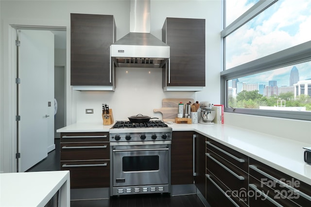 kitchen with luxury stove, a city view, dark brown cabinetry, wall chimney range hood, and light countertops