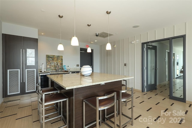 kitchen featuring modern cabinets, light stone countertops, a kitchen bar, a center island, and hanging light fixtures