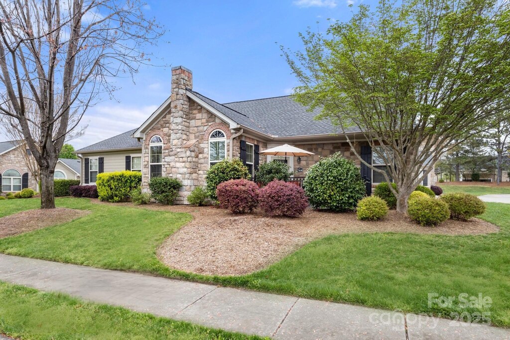 744 Ledgestone Ct, Tega Cay, SC 29708 - view of front facade with stone siding, a chimney, a shingled roof, and a front lawn