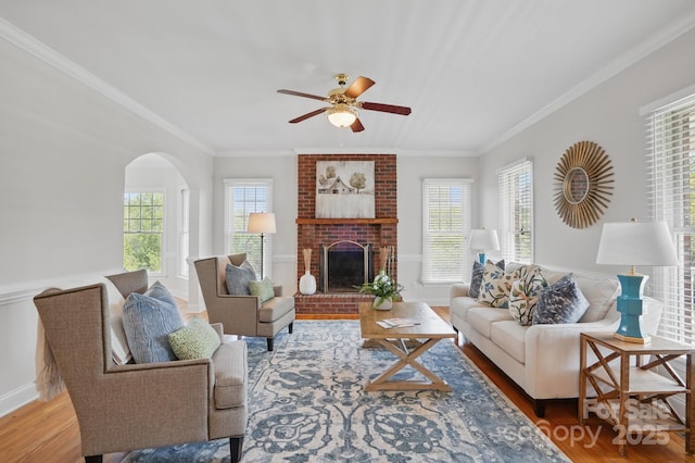 living area featuring crown molding, wood finished floors, ceiling fan, and a healthy amount of sunlight