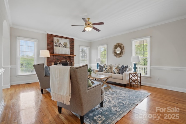 living area featuring wood finished floors, crown molding, baseboards, and ceiling fan