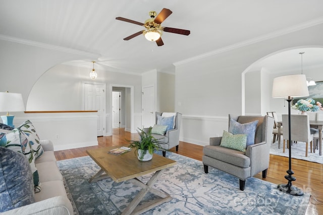 living area with a ceiling fan, wood finished floors, arched walkways, and crown molding