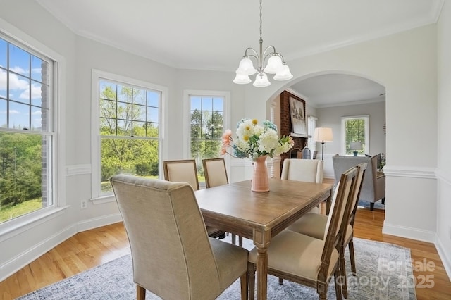 dining room with arched walkways, a healthy amount of sunlight, and light wood finished floors