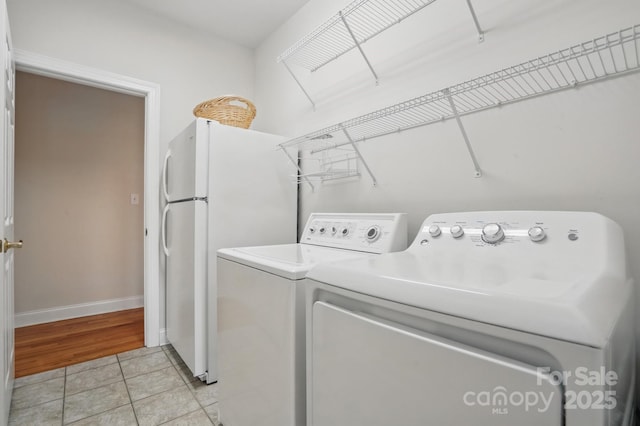 clothes washing area with light tile patterned floors, washing machine and clothes dryer, baseboards, and laundry area