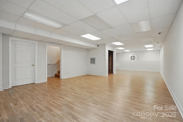 empty room featuring stairs, light wood-type flooring, visible vents, baseboards, and a paneled ceiling