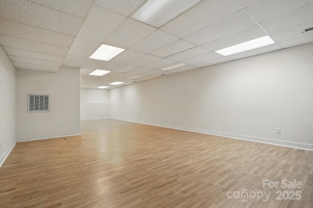 empty room featuring baseboards, a drop ceiling, light wood-style floors, and visible vents