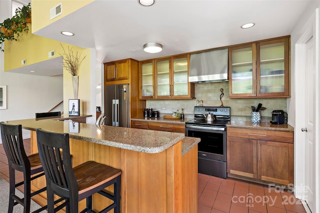 27 Stokes Dr, Asheville, NC 28805 - kitchen featuring appliances with stainless steel finishes, wall chimney exhaust hood, tasteful backsplash, tile patterned floors, and a breakfast bar area