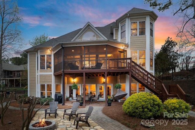 back of property at dusk with a sunroom, an outdoor fire pit, stairway, a shingled roof, and a patio area