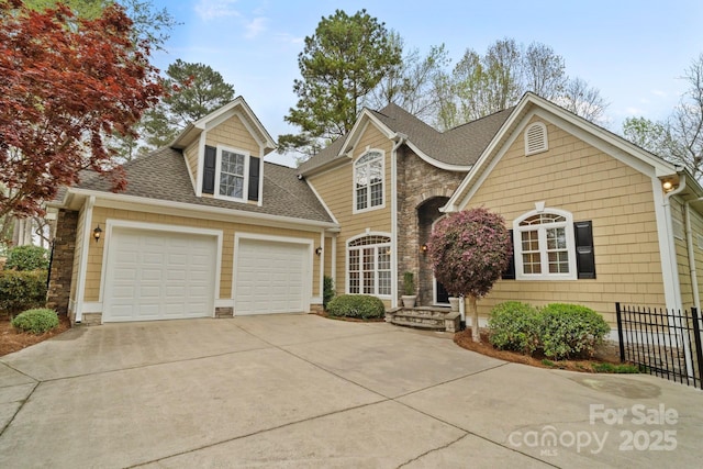 traditional home with stone siding, fence, a garage, driveway, and a shingled roof