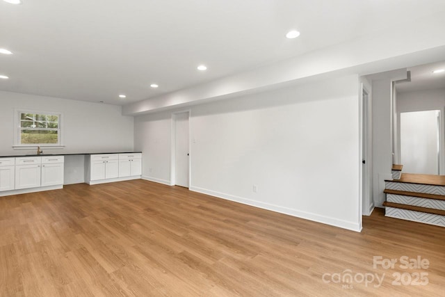 below grade area featuring light wood-style floors, baseboards, recessed lighting, and a sink